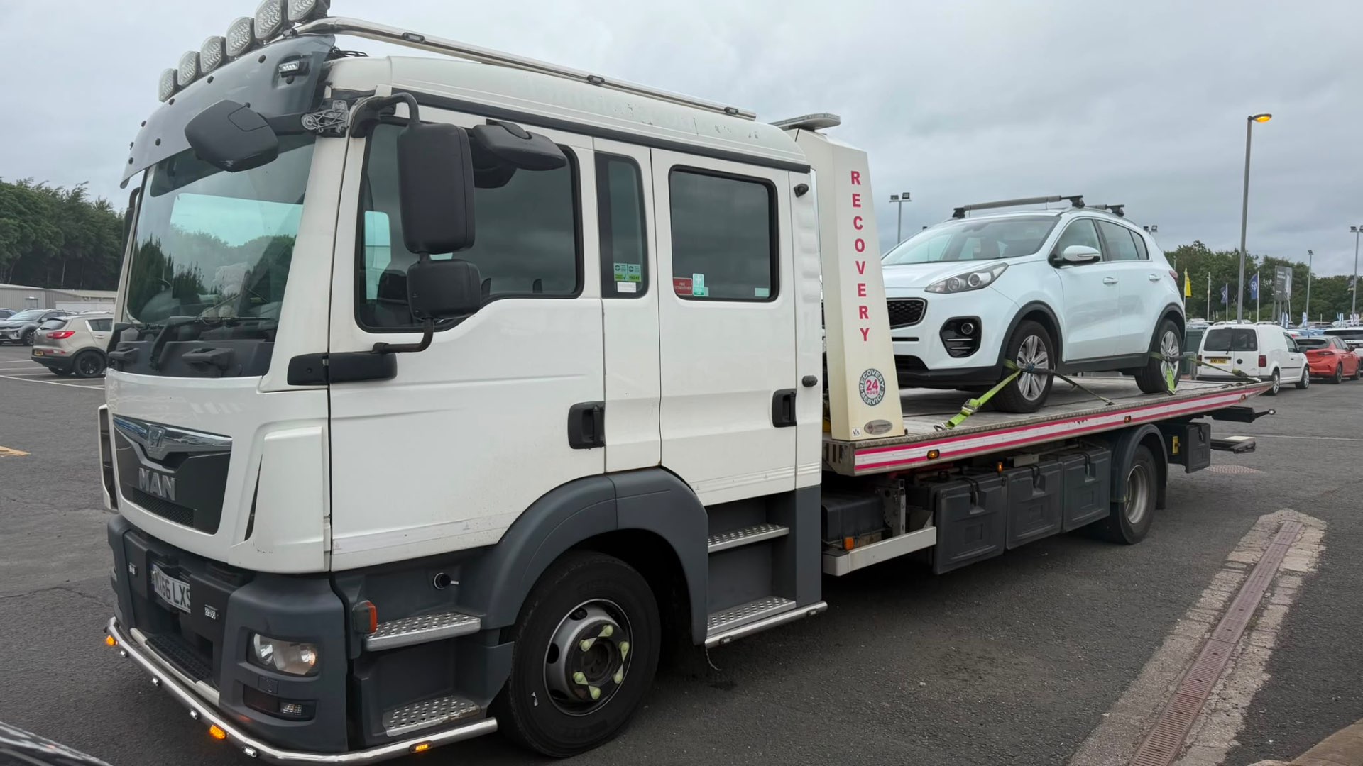 White MAN recovery truck with Kia Sportage on flatbed at dealership
